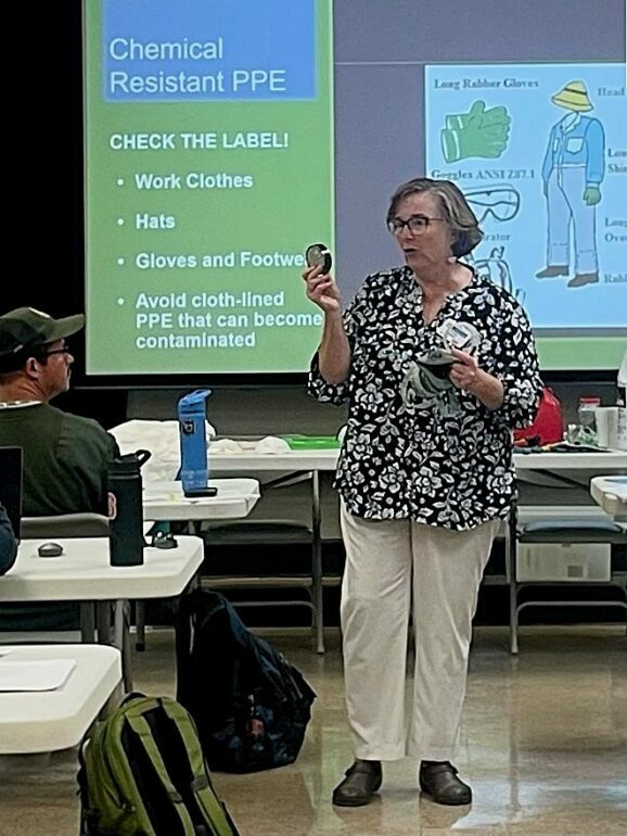 A woman teaching a class about chemical-resistant PPE while holding a respirator mask and cartridge filter